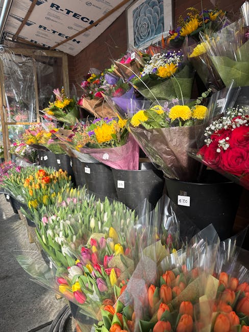 A display of various fresh floral arrangements and bouquets in a flower shop, featuring a wide range of bright, vibrant flowers such as yellow daisies, pink tulips, purple irises, orange tulips, and r